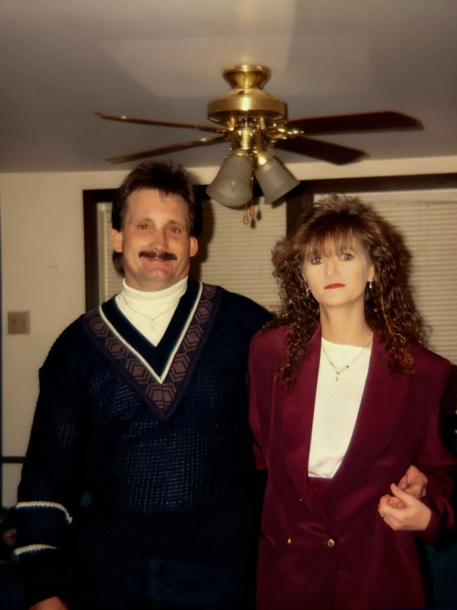 Joshua’s parents standing together indoors, dressed in a dark sweater and burgundy jacket